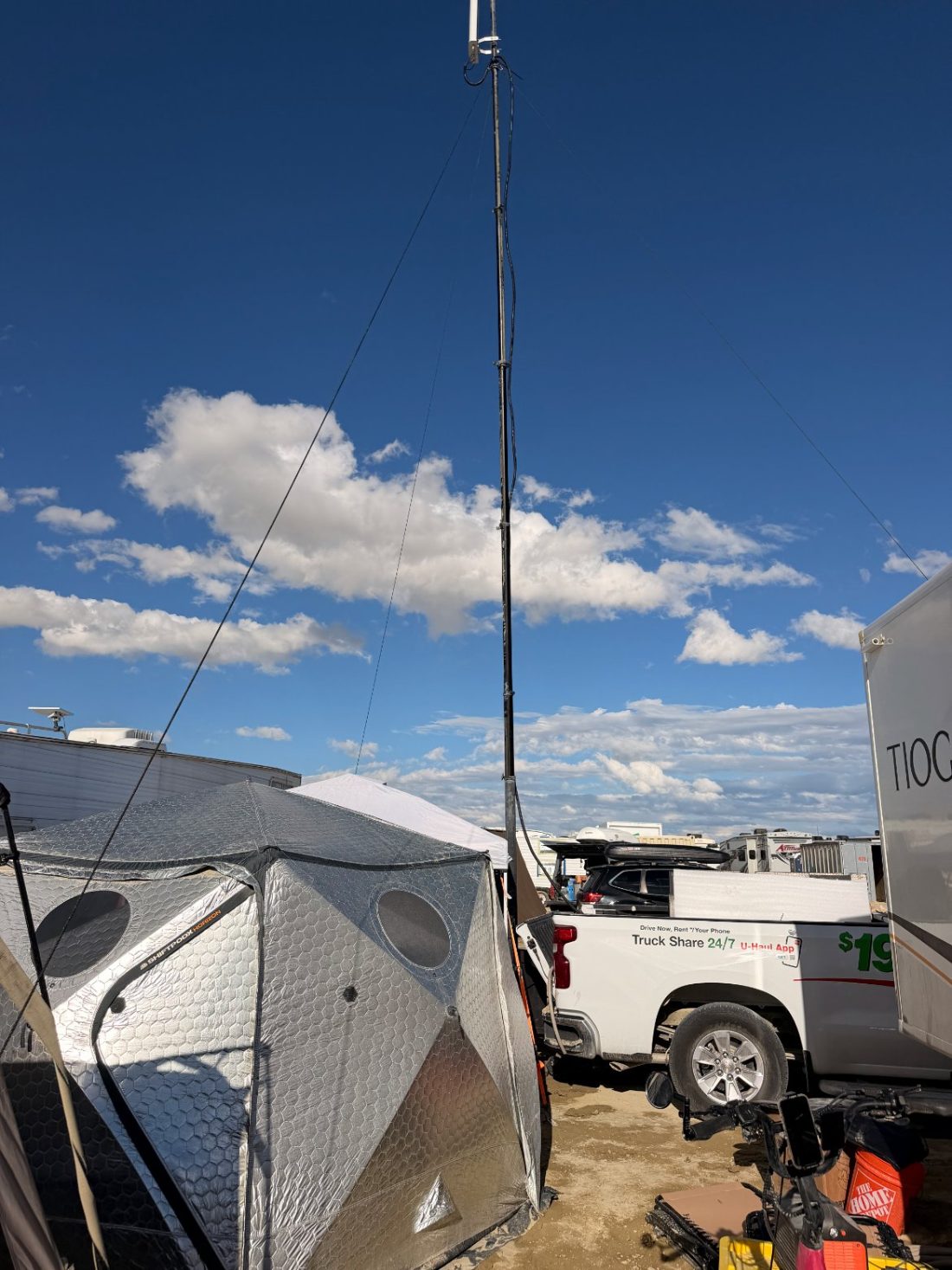 The camp in daylight with the mast standing above it, dust and vehicles across the open playa