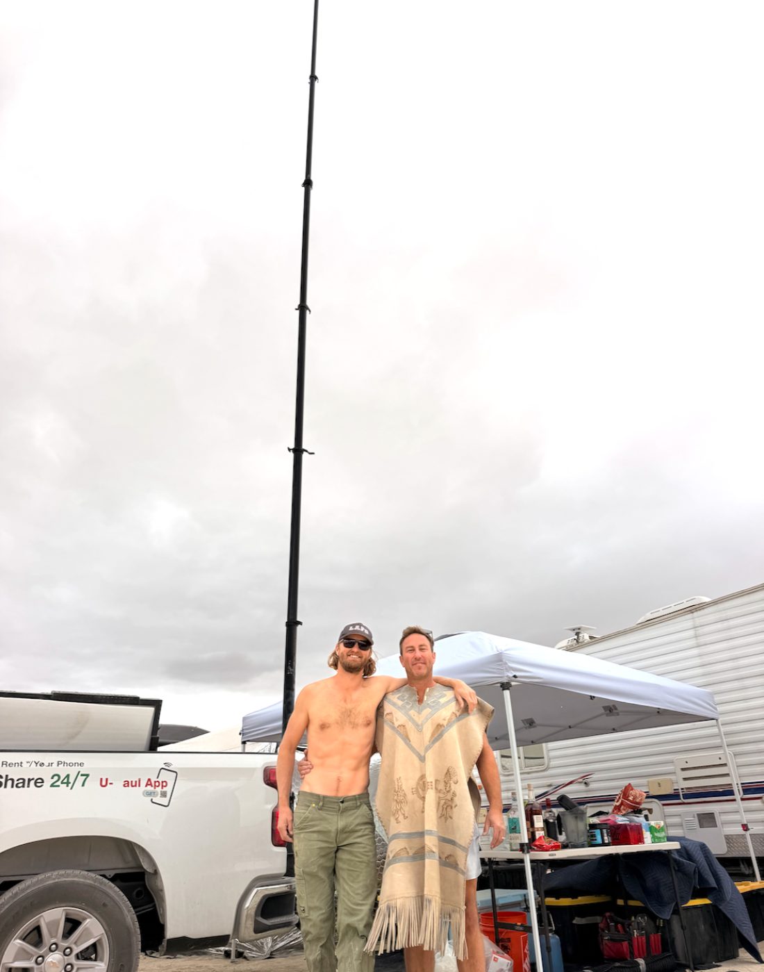 Two people raising the hitch-mounted mast, the full height of it visible against the sky