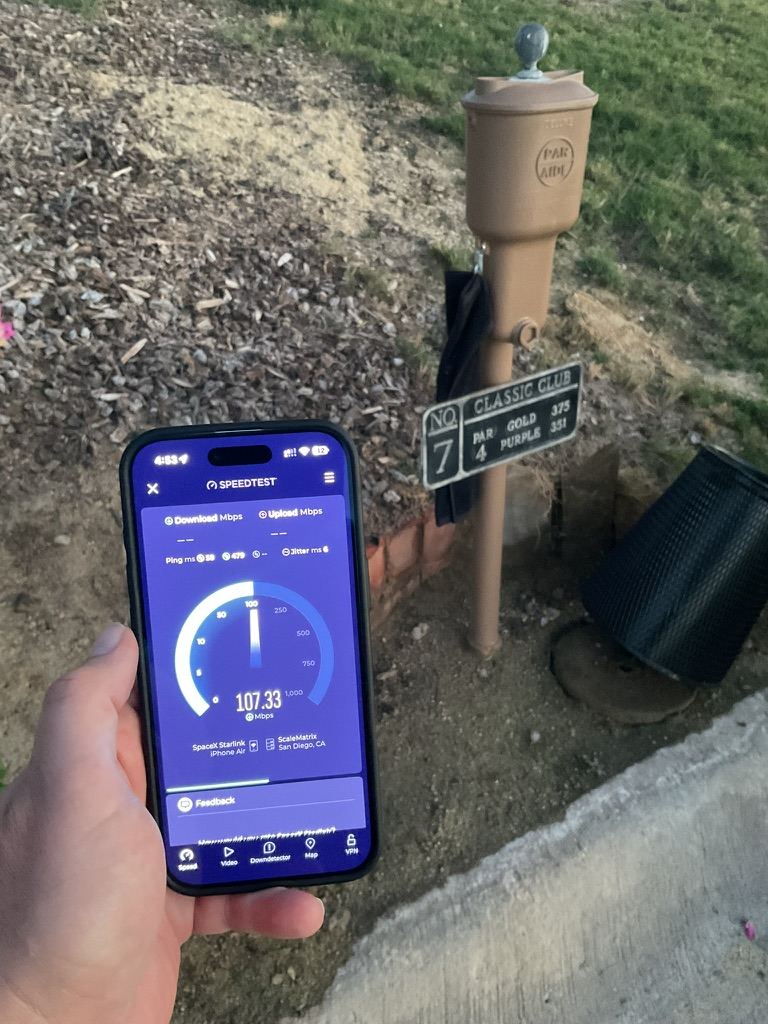 A phone showing a 107 Mbps speed test result, held beside the Classic Club No. 7 tee marker