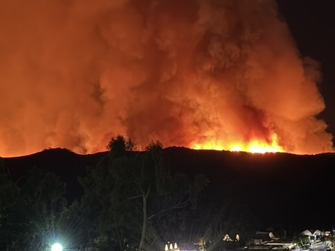 Wall of wildfire and smoke burning along the ridline above the campus at night