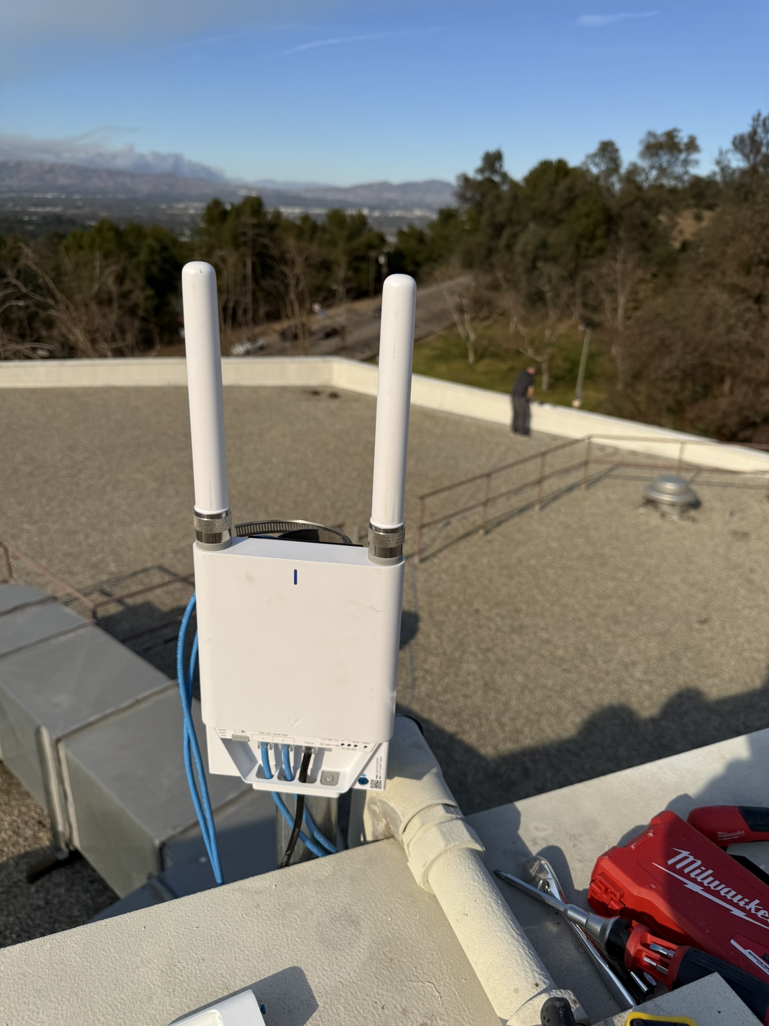 Verkada cellular gateway with dual antennas mounted on a campus rooftop, smoke visible on the horizon