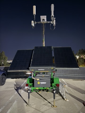 Solar-powered lithium battery cell trailer with antennas and radios at the top, deployed on the Milken East campus at dusk